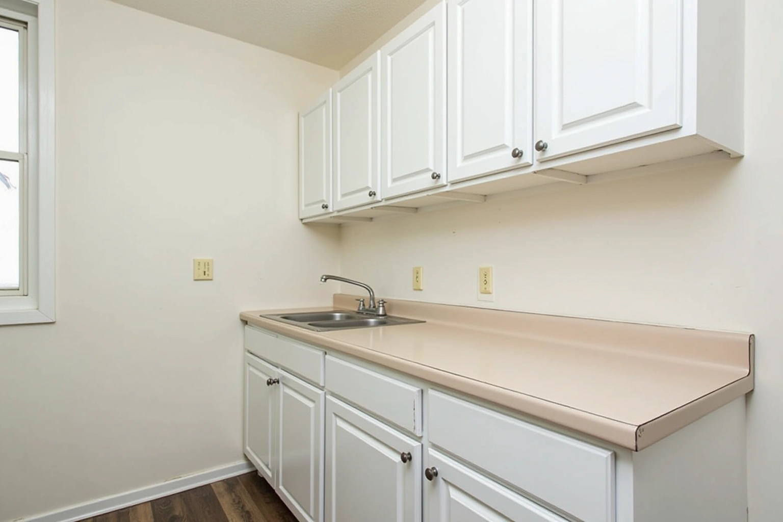 Basic kitchen with white raised-panel stock cabinets, a beige laminate counter, a stainless drop-in sink, and bare walls.