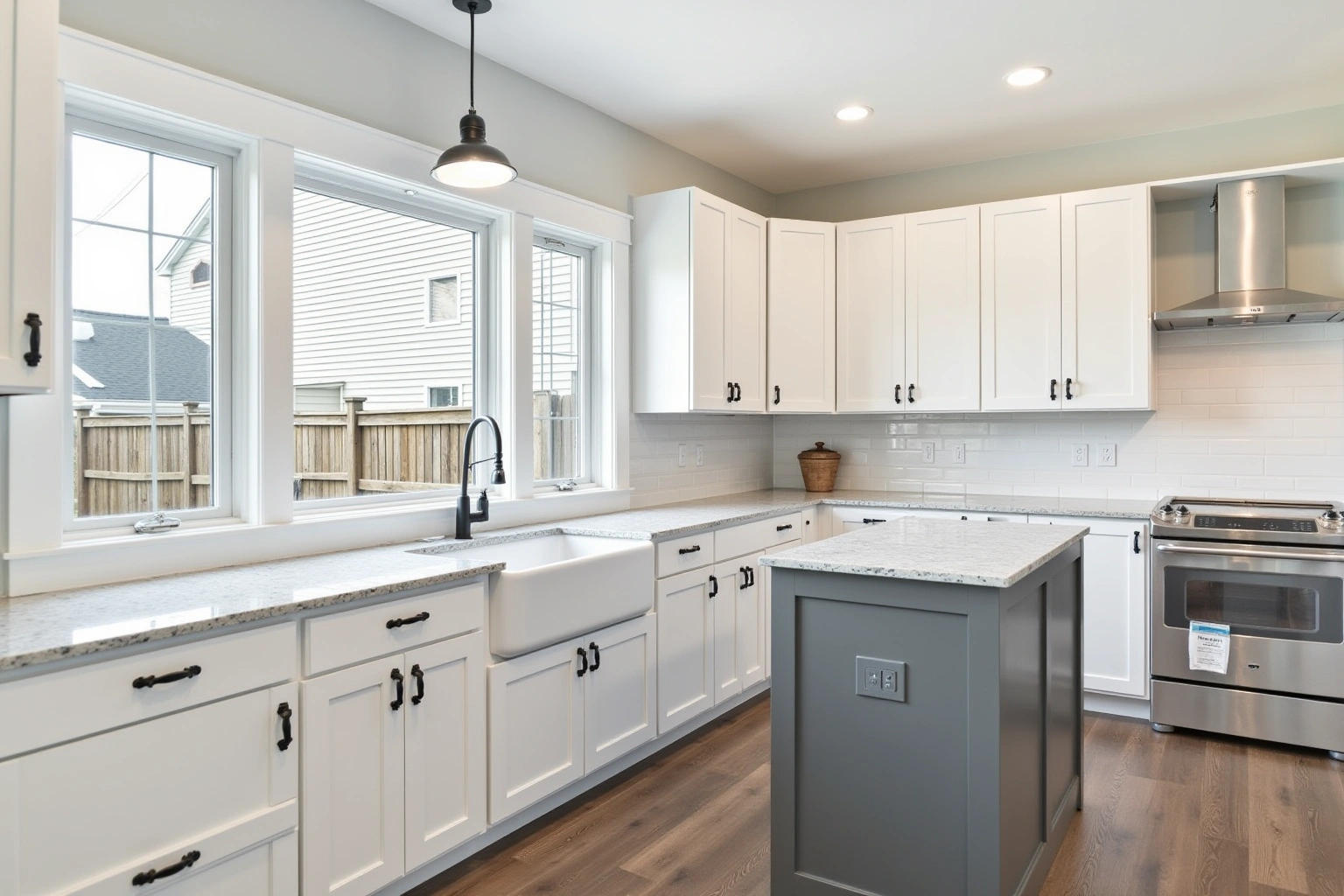 White shaker cabinets with black pulls, a grey island, speckled counters, a farmhouse sink, and subway tile.
