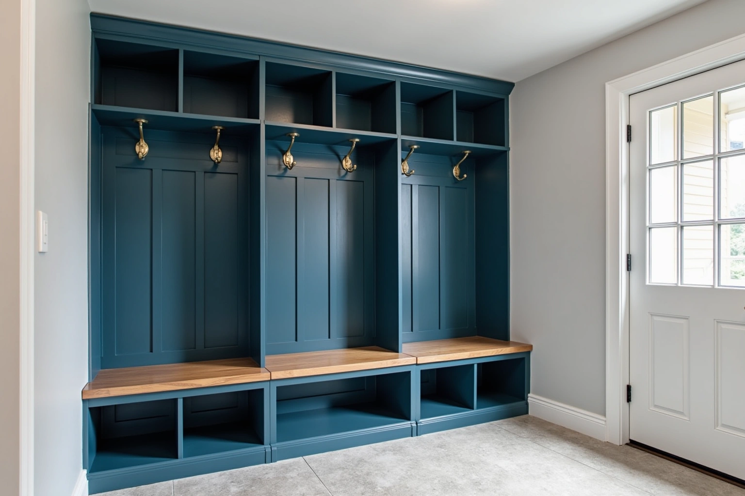 Three deep blue mudroom lockers with a wood bench, brass hooks, and open cubbies beside a glazed door.